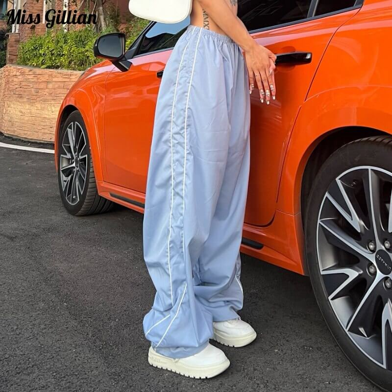 Woman wearing oversized baggy high-waisted sweatpants in light blue, standing beside an orange car.